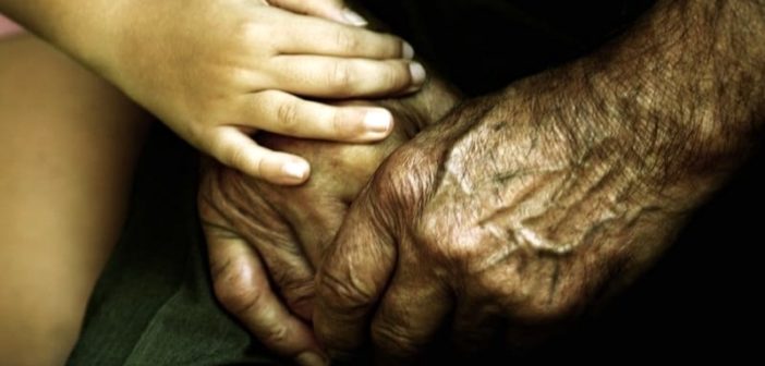 primer plano de un niño que sostiene las manos de un anciano y le muestra compasión