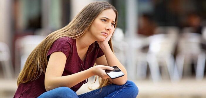 mujer sosteniendo el teléfono con aspecto triste tratando de decidir si debería bloquear a su ex
