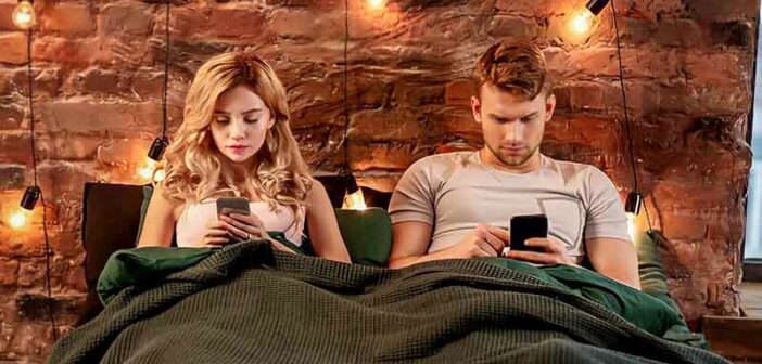 pareja sentada en la cama mirando su teléfono ilustrando los efectos de las redes sociales en las relaciones