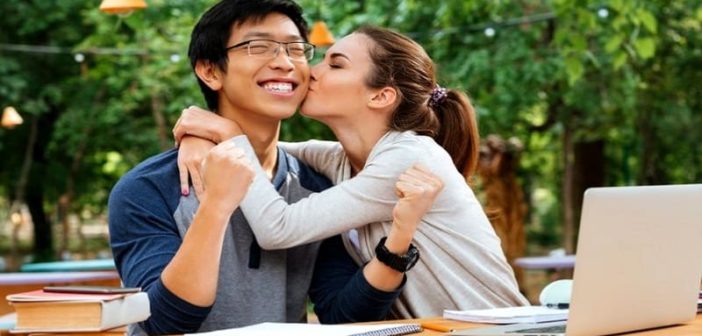 joven asiático siendo besado en la mejilla por una joven atractiva, ilustrando salir de la zona de amigos