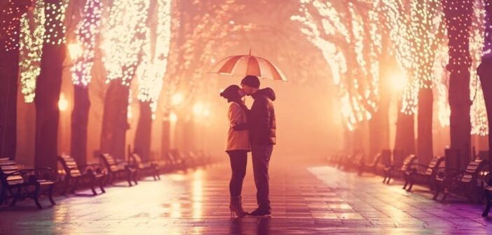 pareja besándose bajo el paraguas por un bulevar con luces