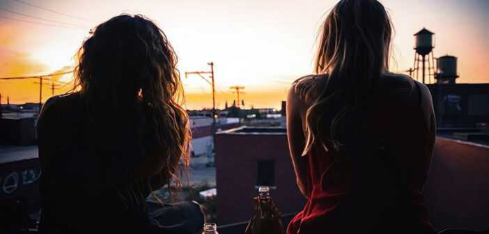 dos amigos hablando mientras miran una puesta de sol sobre una ciudad