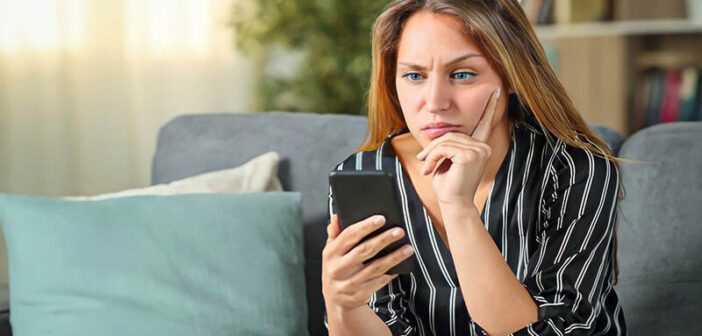 mujer joven confundida mirando su teléfono preguntándose por qué no enviará un mensaje de texto primero