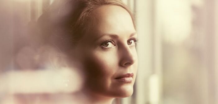 mujer tímida mirando por la ventana ilustrando la necesidad de ser más abierta hacia las personas