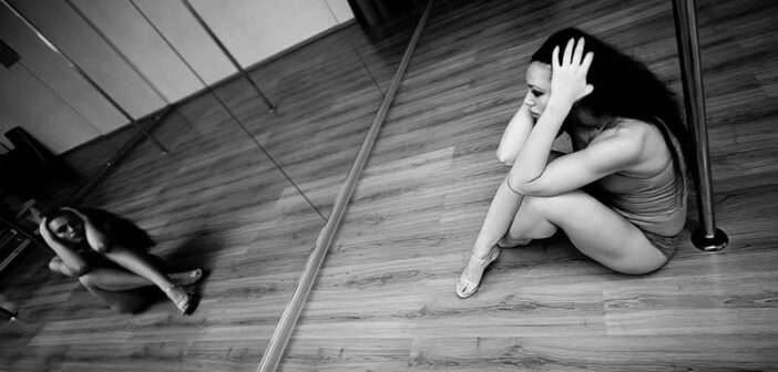 mujer en un estudio de danza sentada en el suelo con aspecto triste - ilustrando el intento de mantenerse positiva en un mundo negativo